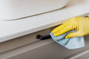 About From above of crop faceless person in yellow gloves cleaning handle of cabinet with microfiber cloth in modern bright bathroom