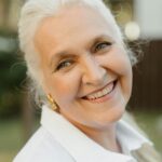 Home A joyful senior woman with gray hair and a warm smile outdoors.