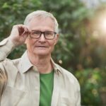Home Senior man adjusting glasses in a sunny outdoor setting with greenery.